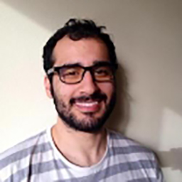 Homme souriant avec lunettes et barbe, portant chemise à carreaux.